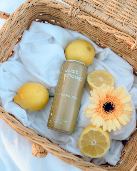 Can of Chardonnay from Just Enough Wines in a picnic basket with lemon and flowers.