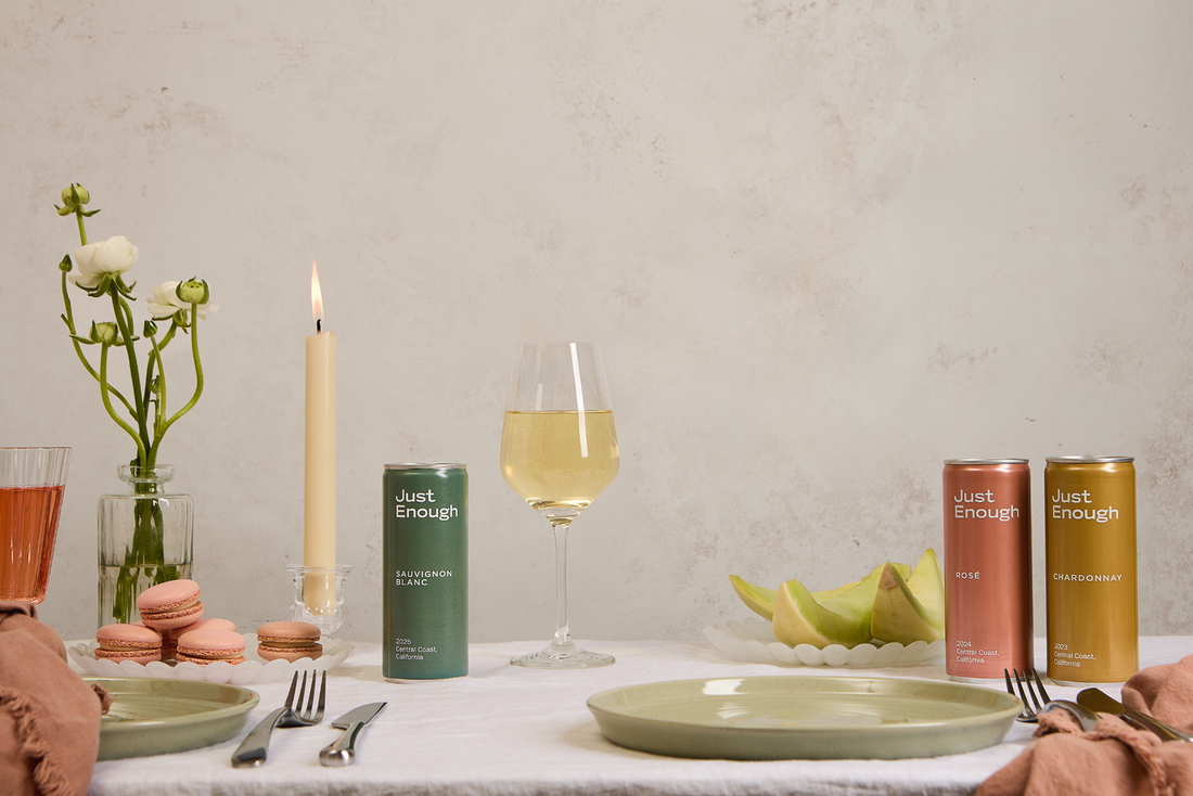Three cans of Just Enough wines beside two filled glasses and a candle on an Easter dining table