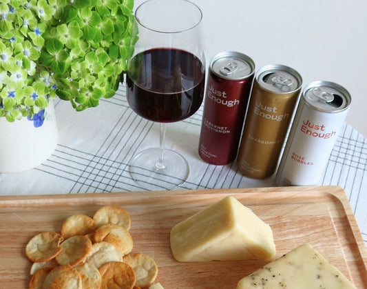 A romantic display featuring Just Enough Wine Red Blend cans beside a glass of poured wine, set against a warm, intimate backdrop.