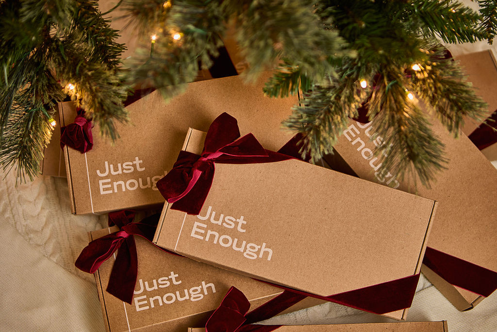Stacked Just Enough Wines gift boxes tied with burgundy velvet ribbons under a decorated Christmas tree.