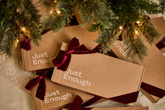 Stacked Just Enough Wines gift boxes tied with burgundy velvet ribbons under a decorated Christmas tree.