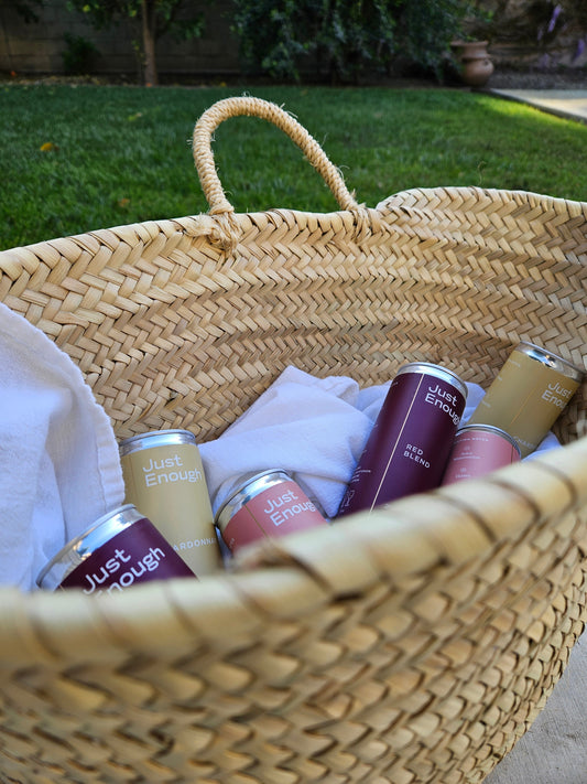 Jute basket filled with Just Enough canned wines, wrapped in a white cloth, highlighting eco-friendly gift presentation.
