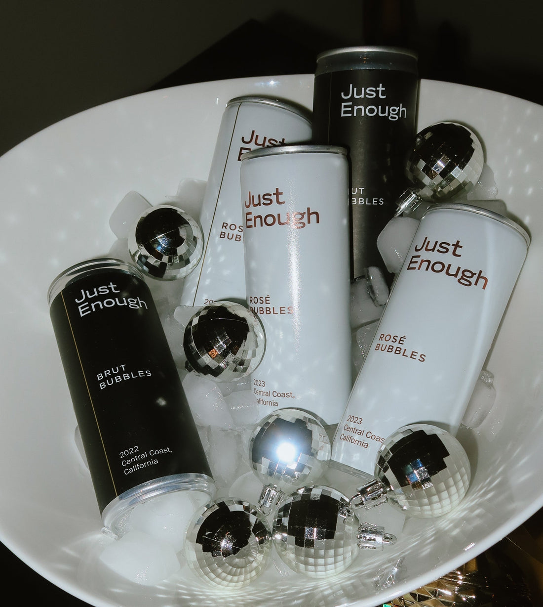 Cans of Just Enough Rosé Bubbles and Brut Bubbles nestled in a bowl with disco balls, styled for Valentine’s week.
