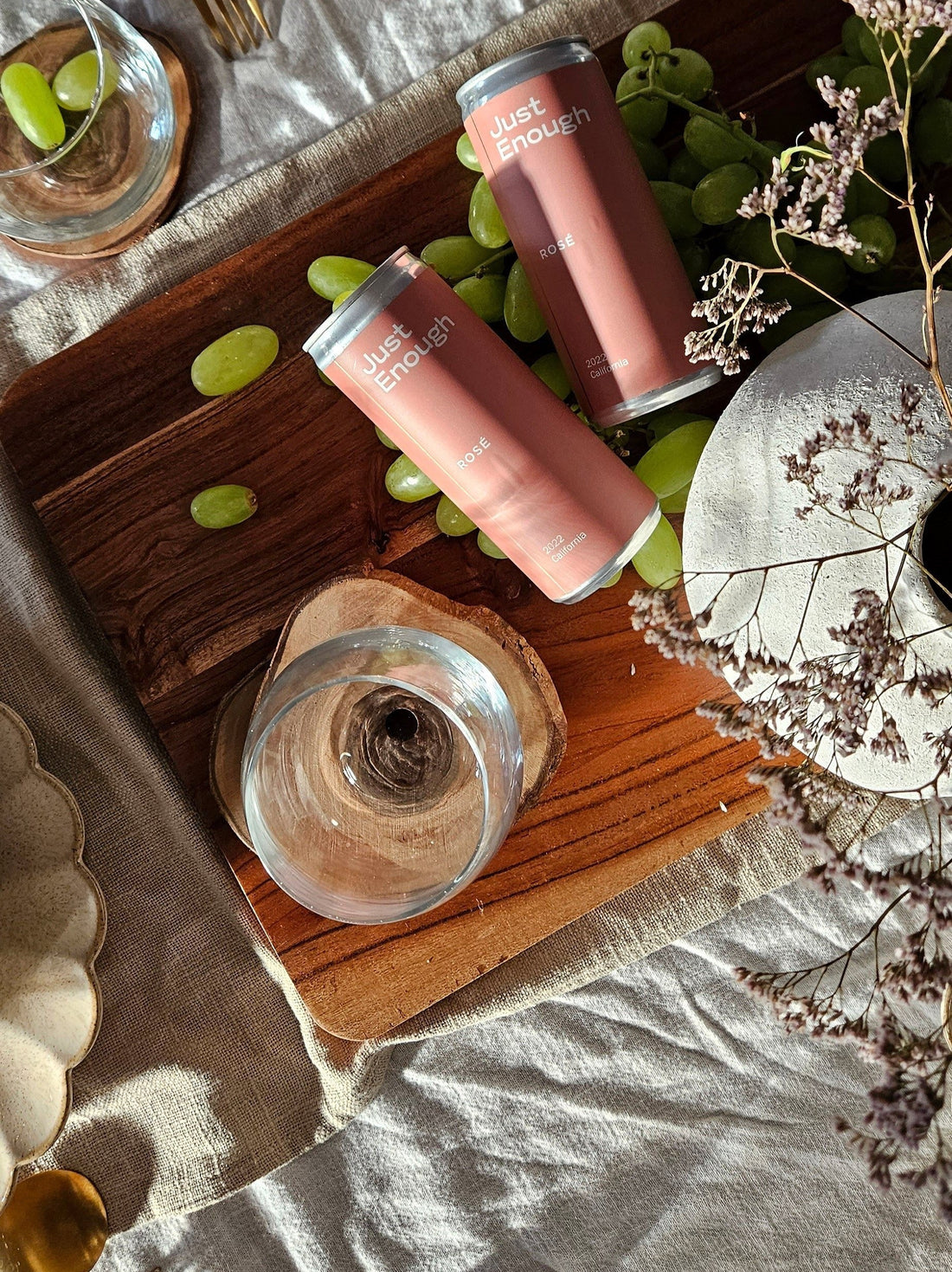 Overhead shot of two Just Enough Rosé cans and green grapes on a wooden cutting board.