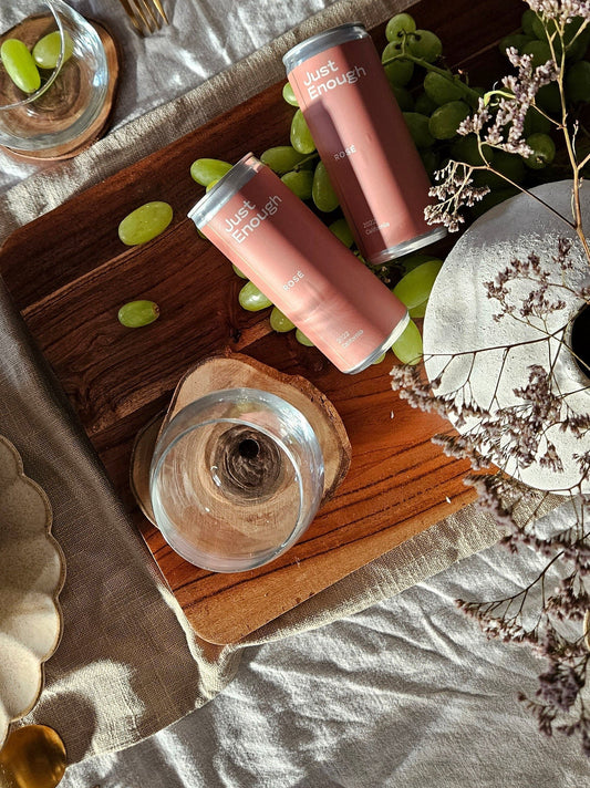 Overhead shot of two Just Enough Rosé cans and green grapes on a wooden cutting board.