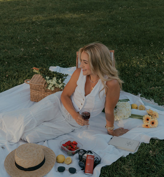 Woman relaxing in a park beside a can of Just Enough Wines during an outdoor picnic.