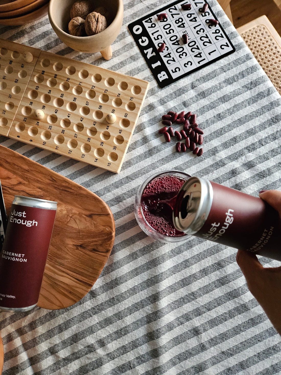Person pouring red wine from a Just Enough canned wine into a glass at an outdoor BBQ