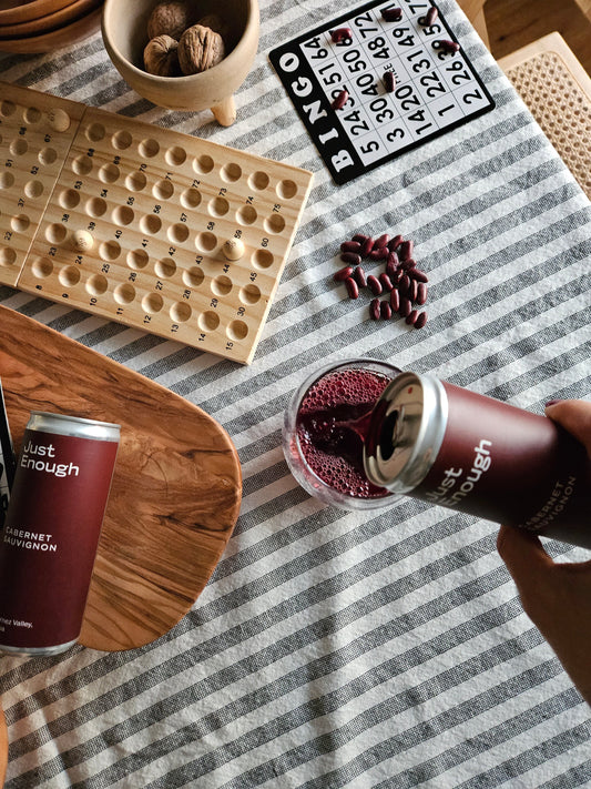 Person pouring red wine from a Just Enough canned wine into a glass at an outdoor BBQ