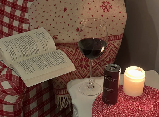 An open book, an opened can of Cabernet Sauvignon from Just Enough Wines, and a burning candle near a sofa. 